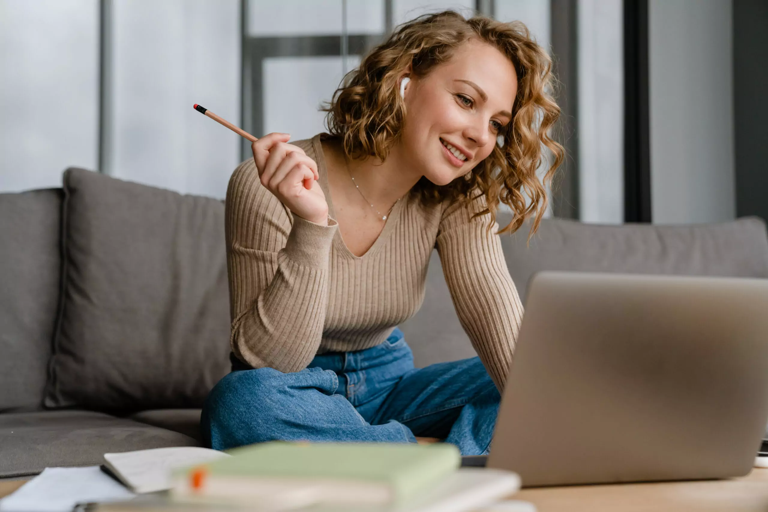 Jeune femme souriante avec écouteurs, travaillant sur son laptop — formation en ligne L'École Virtuelle